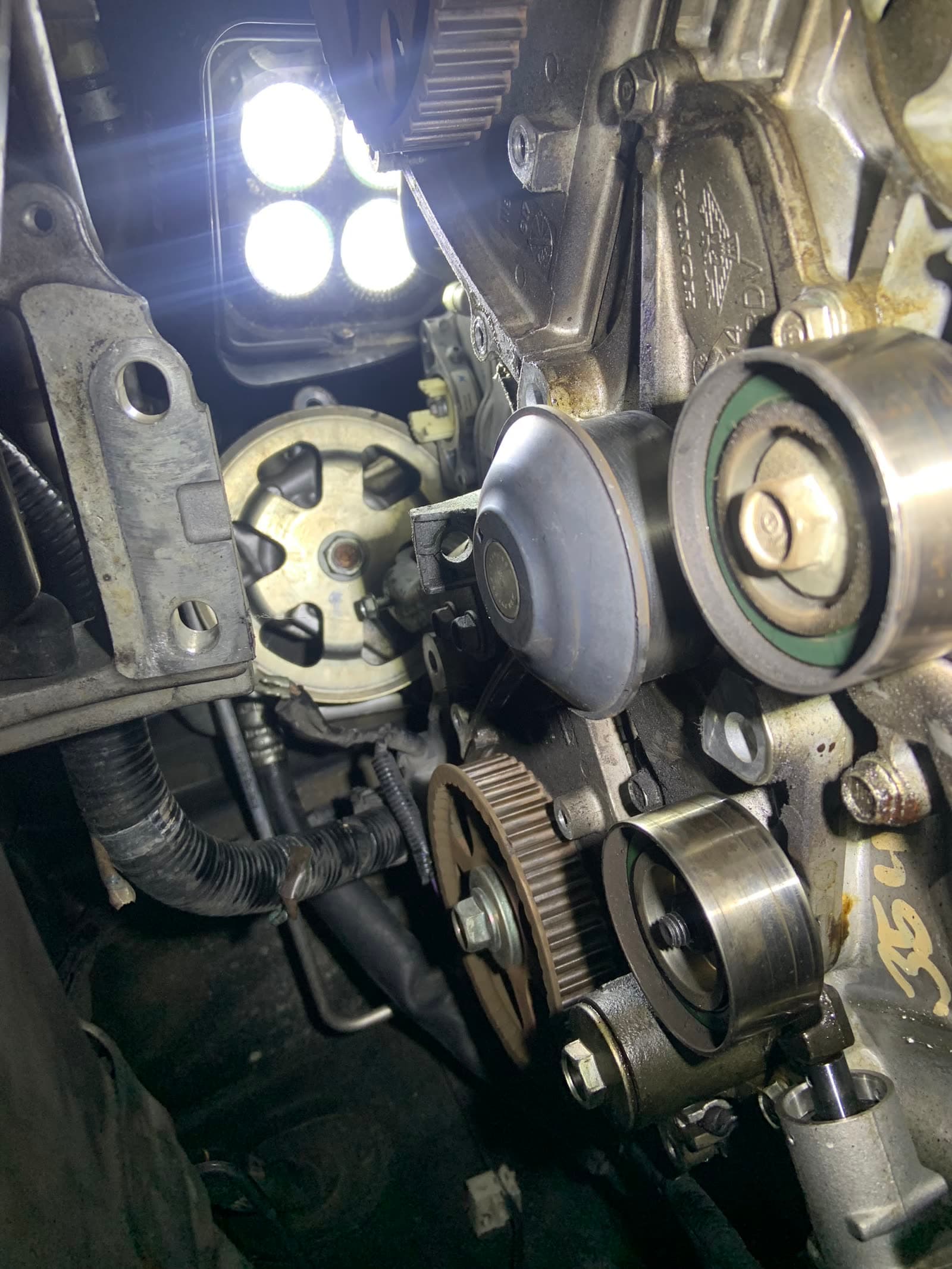 A timing belt service in progress on a Honda engine, lit by a work light