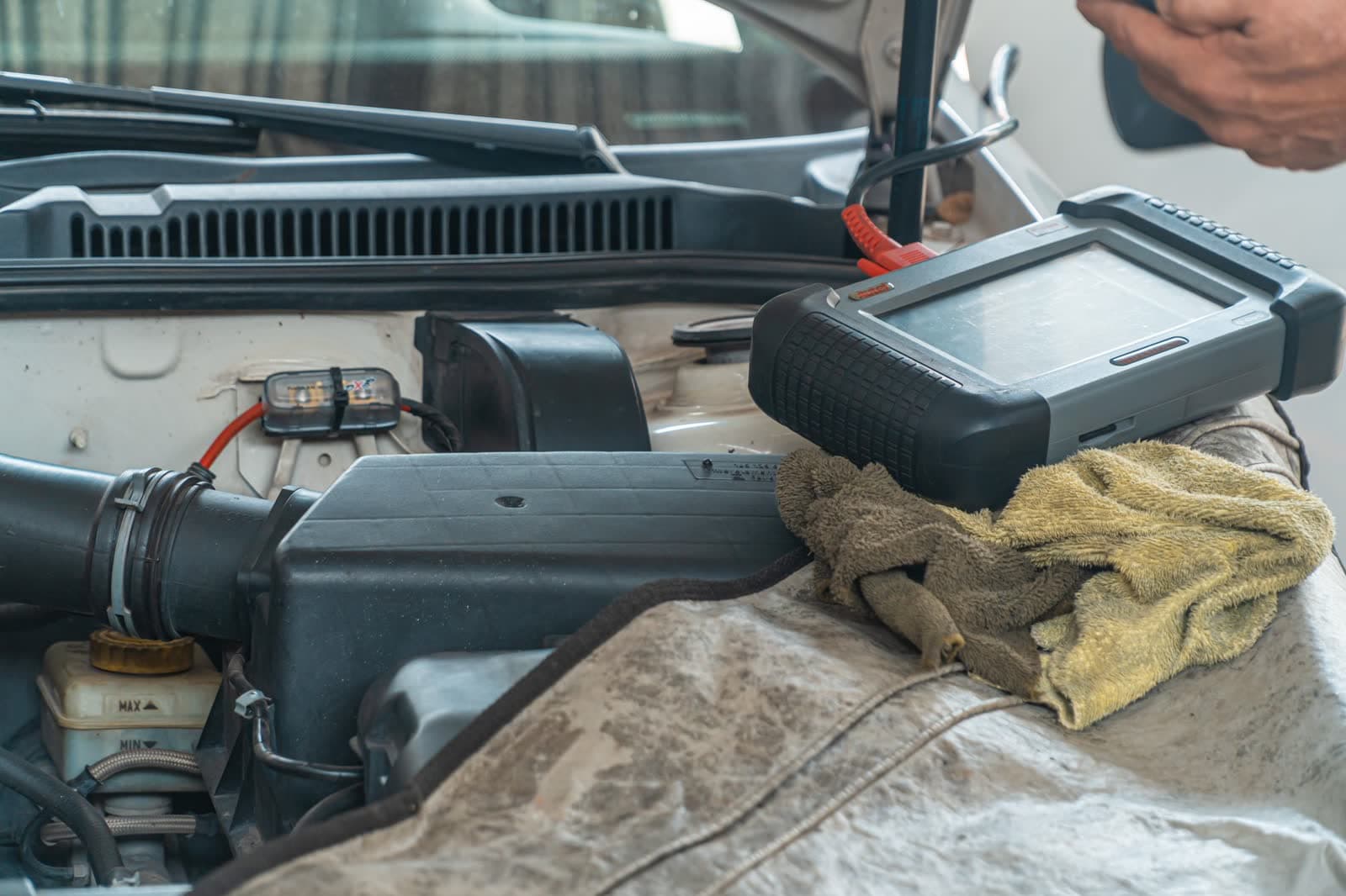 A professional scan tool resting on a fender cover over an open engine bay