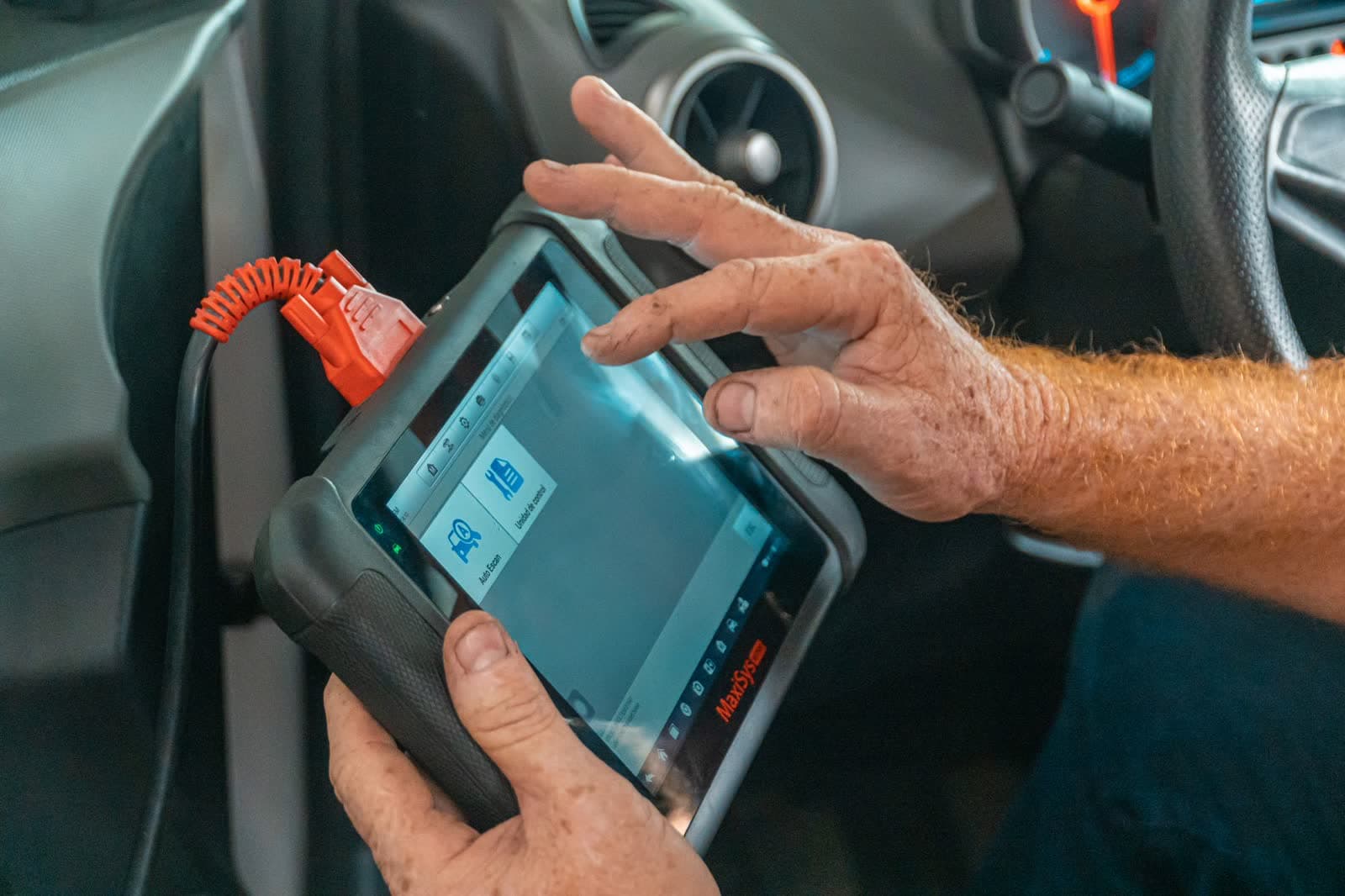 Hands holding a diagnostic scan tool plugged into a vehicle