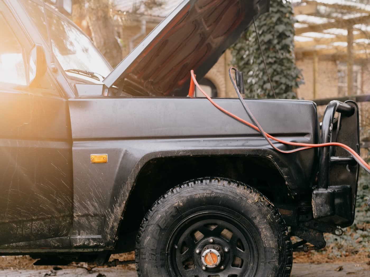 Jumper cables clamped to a battery under an open vehicle hood outdoors